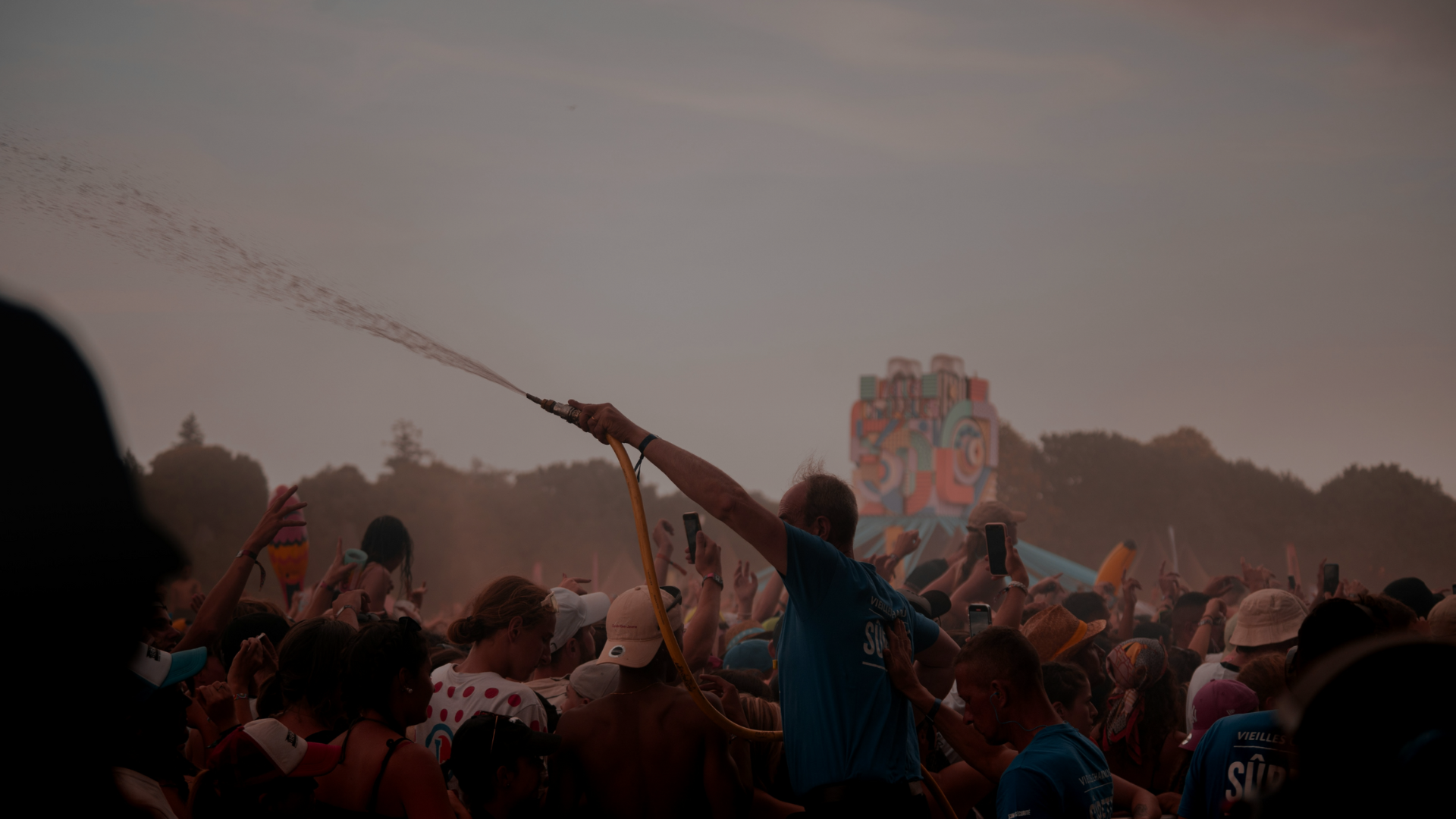 Dette er til en koncert, hvor en mand i blå t-shirt står med slange, hvor der skydes øl ud af.